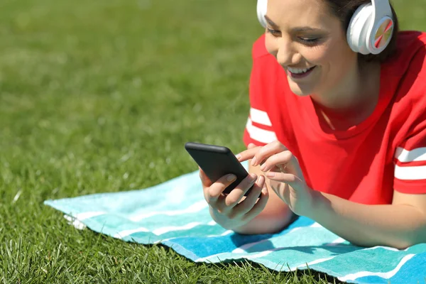 Menina feliz ouve música navegando conteúdo do telefone na grama — Fotografia de Stock