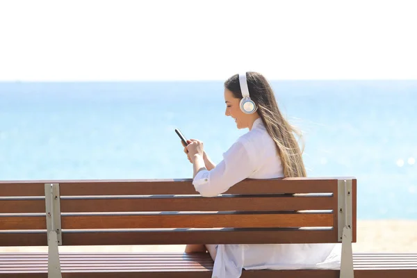 Дівчина слухає музику за допомогою телефону на пляжі — стокове фото