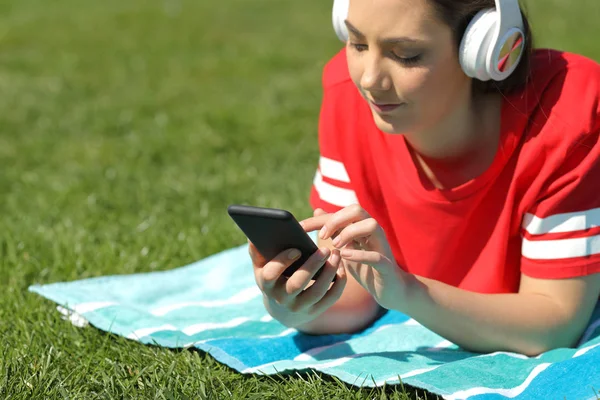 Menina séria ouve música navegando conteúdo do telefone na grama — Fotografia de Stock