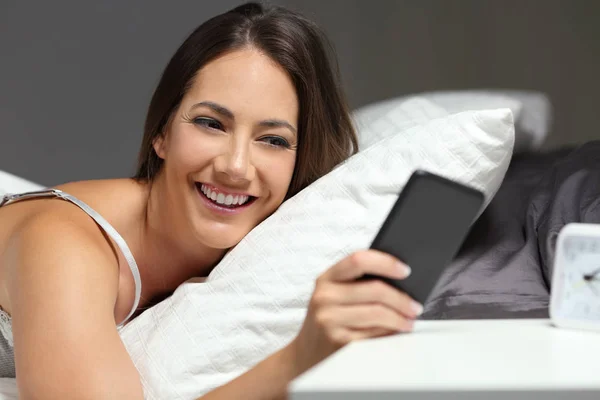 Happy woman on the bed checking phone in the night