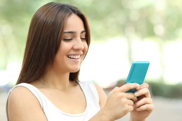 Happy teen checks smart phone walking in the street — Stock Photo, Image