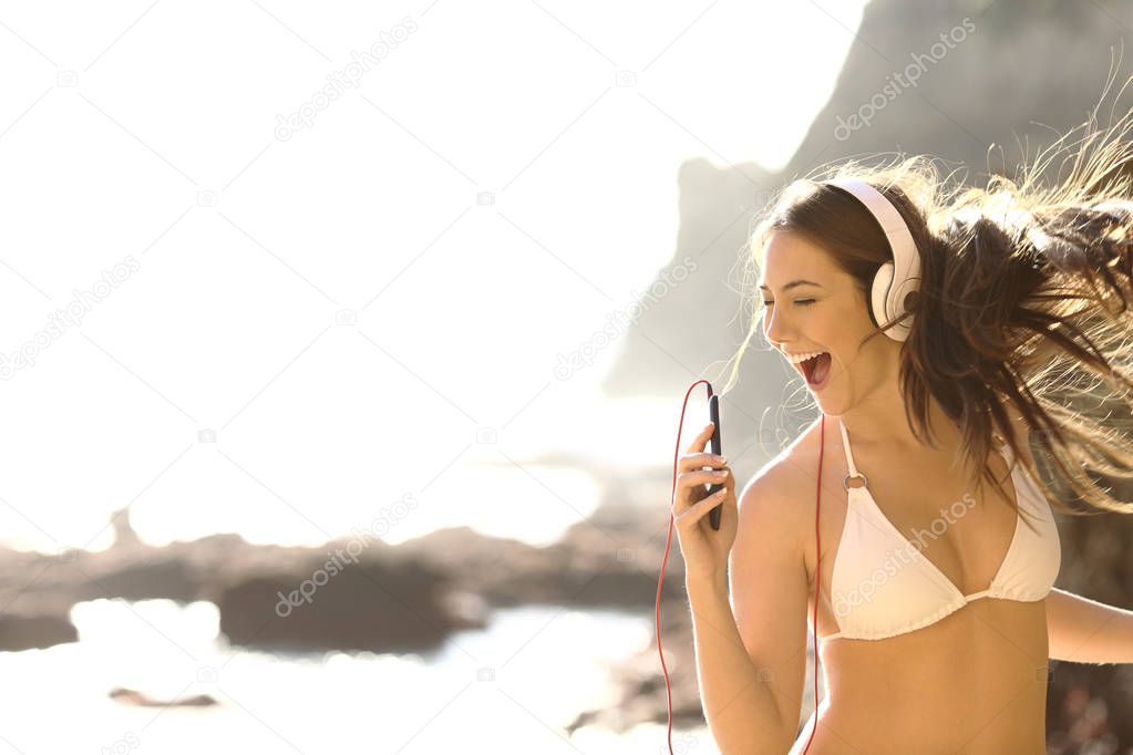 Happy tourist in bikini listens to music and sings songs
