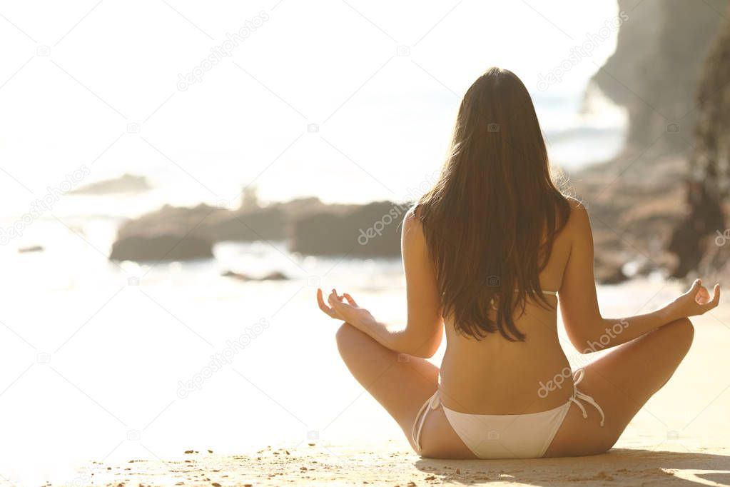 Back view of a woman practicing yoga on the beach