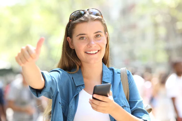 Szczęśliwy nastolatek trzyma telefon wskazując kciuka w górę — Zdjęcie stockowe