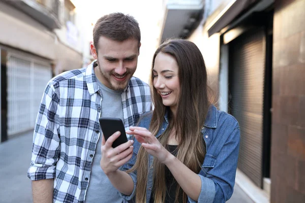 Dos amigos navegando contenido del teléfono caminando por la calle — Foto de Stock