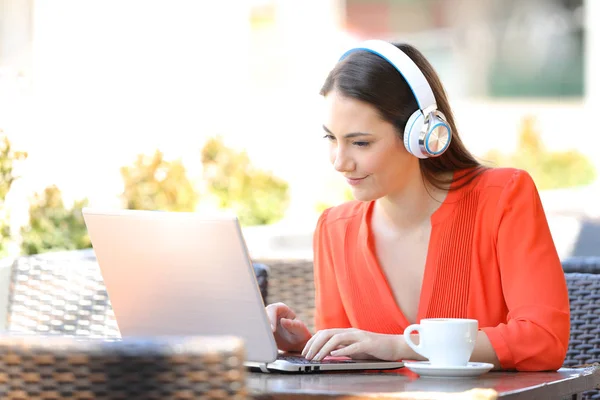 Mulher com fones de ouvido usando um laptop em uma cafeteria — Fotografia de Stock