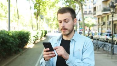 Memnun adam sokakta akıllı telefon kullanır ve bir süre sonra başparmak aşağı kamera bakar