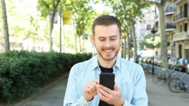 Front view of happy man using smart phone in the street of a big city