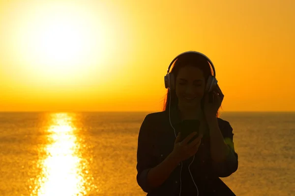 Жіночий силует слухає музику на заході сонця на пляжі — стокове фото