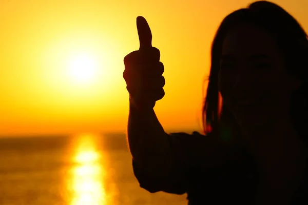 Kvinna siluett gestikulerande tumme upp vid solnedgången — Stockfoto