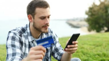 Şaşkın adam kredi kartı ve akıllı telefon ile açık havada ödeme