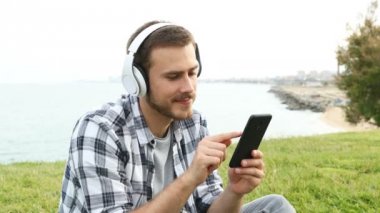 Mutlu adam çim üzerinde oturan akıllı telefon açık havada online medya izlerken