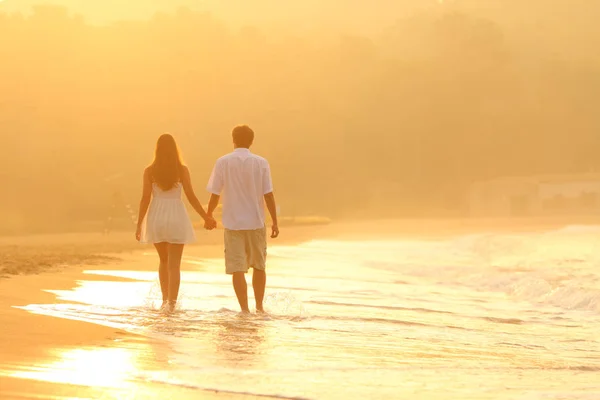 Vista posteriore di una coppia al tramonto passeggiando sulla spiaggia — Foto Stock