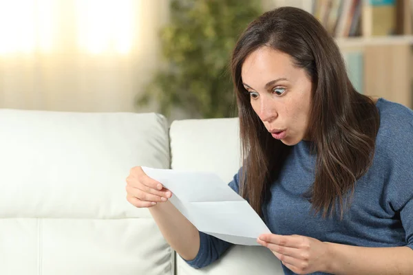 Surprised woman reading a letter on a couch at home — Stock Photo, Image