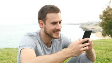 Mutlu adam çim üzerinde oturan açık havada akıllı telefon mesajlaşma
