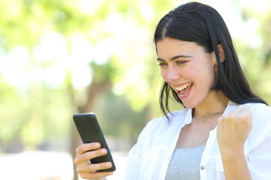 Heyecanlı yetişkin kadın bir parkta telefon içeriği okuma
