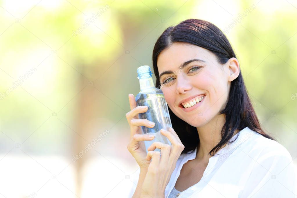 Happy woman holding a bottle of water looking at you