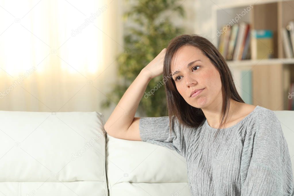 Pensive woman looking away on a couch at home