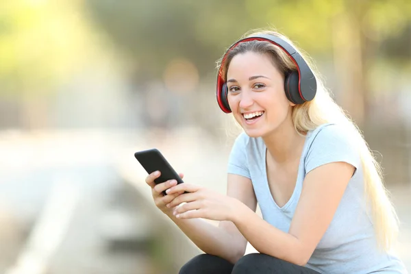 Happy teenage girl listening to music looking at camera — Stock Photo, Image