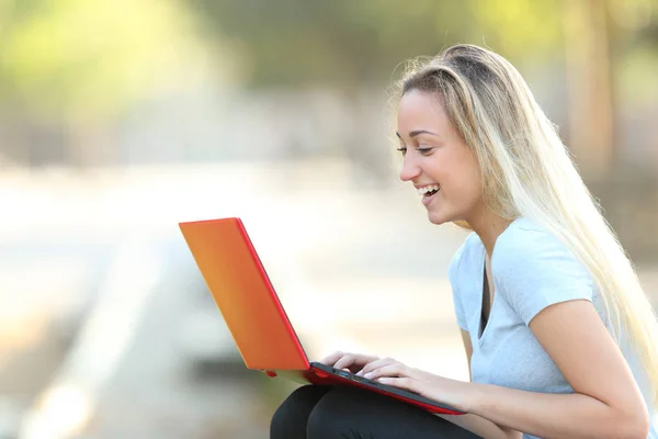 Gelukkig tiener meisje met behulp van een rode laptop in een park — Stockfoto