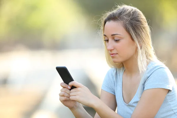 Seriózní mladá dívka kontroluje obsah telefonu v parku — Stock fotografie