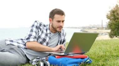 Mutlu adam kulaklık koyarak ve dizüstü bilgisayar çim üzerinde yatan e-öğrenme