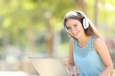 Bir dizüstü bilgisayar ve kulaklık kullanarak Mutlu kadın size bakar