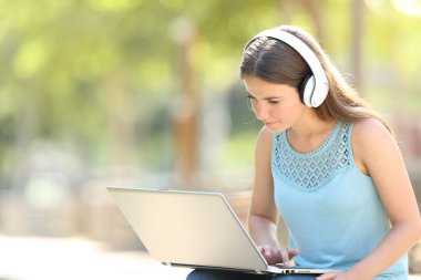 Bir parkta dizüstü bilgisayar ve kulaklık kullanan ciddi bir kadın