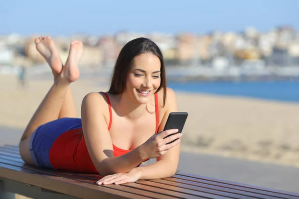Gelukkige tiener in het rood met behulp van slimme telefoon op het strand — Stockfoto
