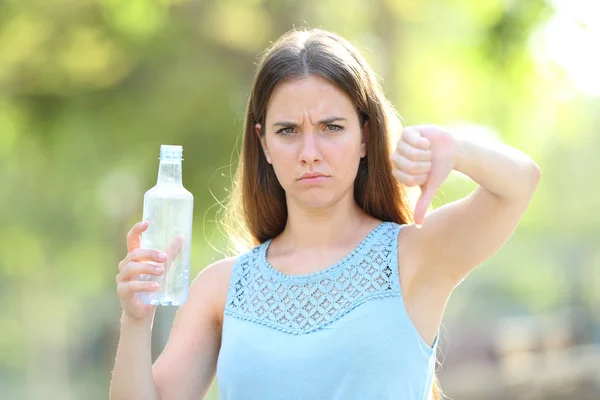 Mulher irritada segurando uma garrafa de plástico com os polegares para baixo — Fotografia de Stock