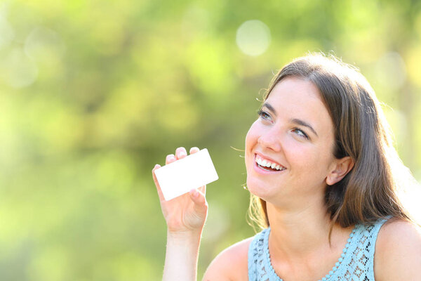 Happy woman showing blank credit card looking at side