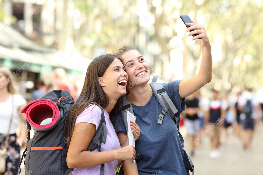 Two happy backpackers taking selfies in the street on vacation