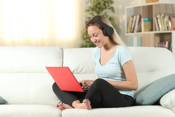 Ragazza felice utilizzando un computer portatile e cuffie su un divano — Foto Stock