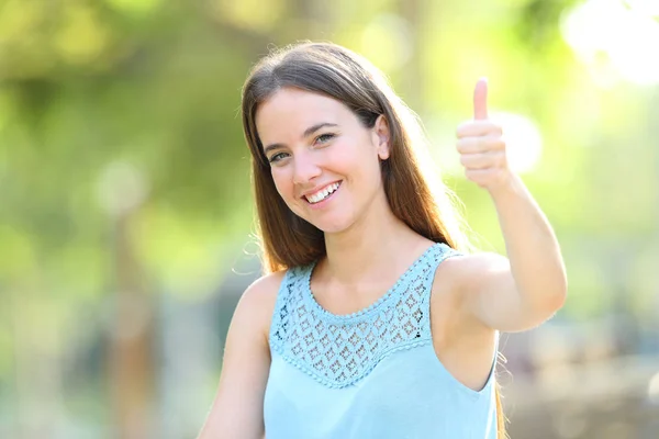 Счастливая женщина на зеленом жесте показывает большие пальцы вверх в парке — стоковое фото