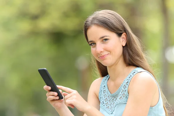 Mujer sonriente sosteniendo el teléfono inteligente mirándote en verde — Foto de Stock
