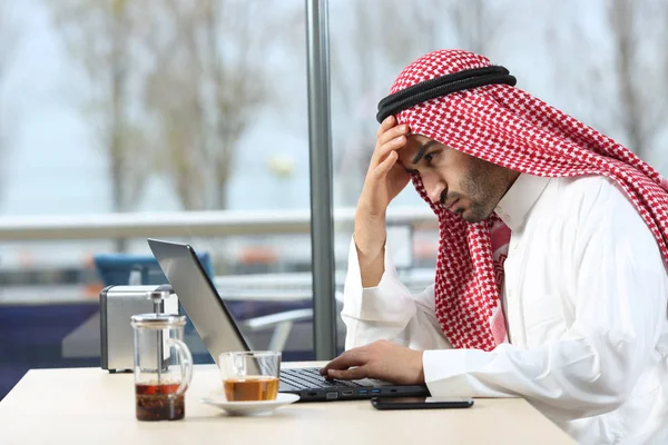 Confused arab man checking laptop in a bar — Stock Photo, Image