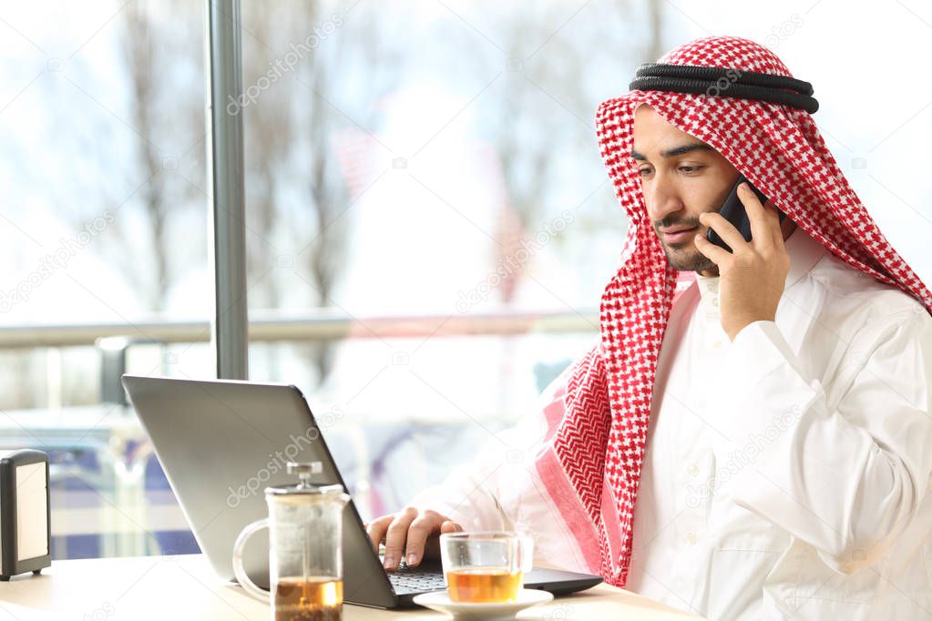 Arab man using a laptop and talking on phone in a bar