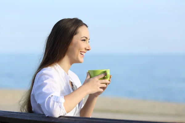 Женщина держит кофе и смотрит на пляж — стоковое фото