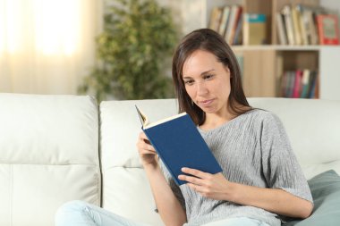 Evde kağıt kitap okuyan ciddi bir kadın