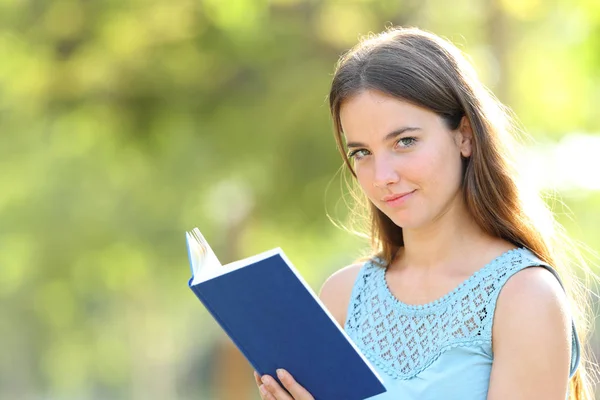Serious woman looks at camera holding a book — Stock Photo, Image