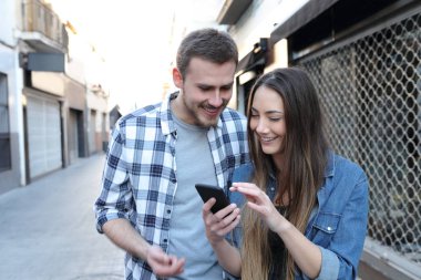 Mutlu çift sokakta akıllı telefon içeriğini kontrol