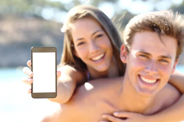 Feliz pareja en la playa mostrando la pantalla del teléfono en blanco — Foto de Stock