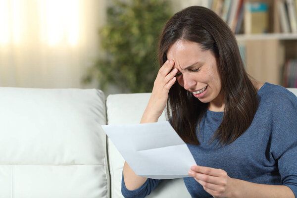 Sad woman reading a letter on a couch at home