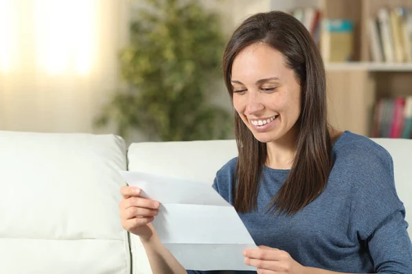 Счастливая женщина читает письмо на диване дома — стоковое фото