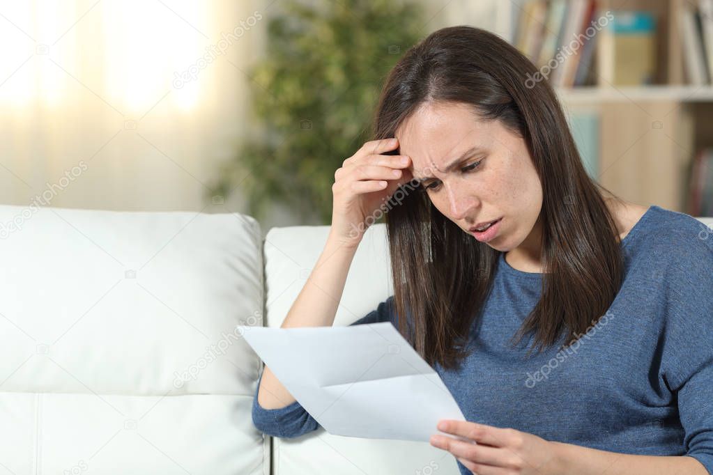 Worried woman reading a letter on a couch at home