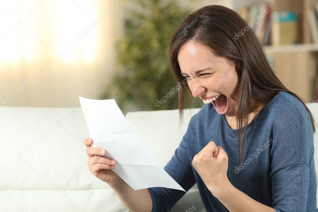 Excited woman reading a letter on a couch at home