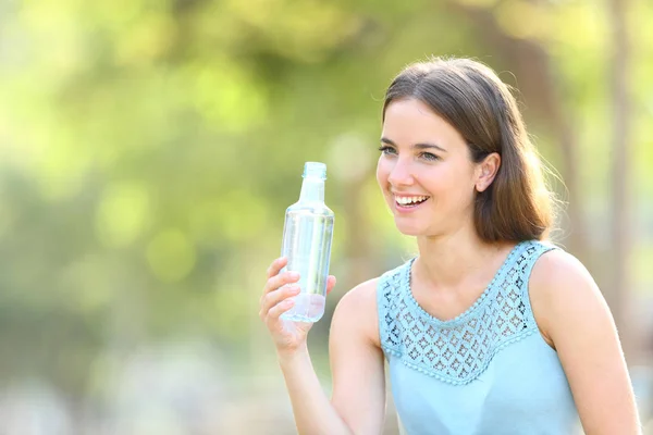 Счастливая женщина держит пластиковую бутылку воды на зеленом — стоковое фото