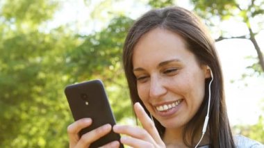 Mutlu yetişkin kadın kulaklık ve telefon ile müzik dinlerken ve bir parkta dans