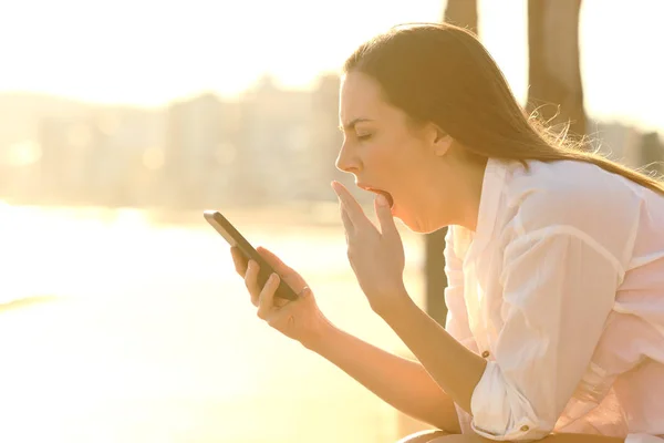Trött kvinna som använder telefon gäspningar på stranden — Stockfoto