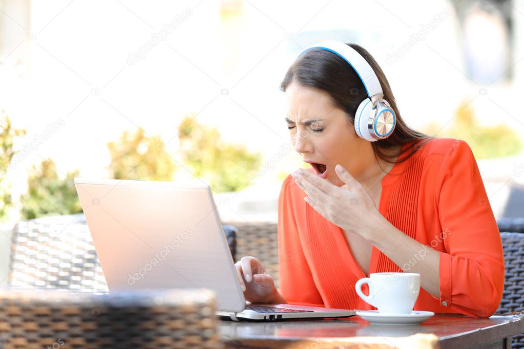 Tired woman yawning using a laptop in a bar